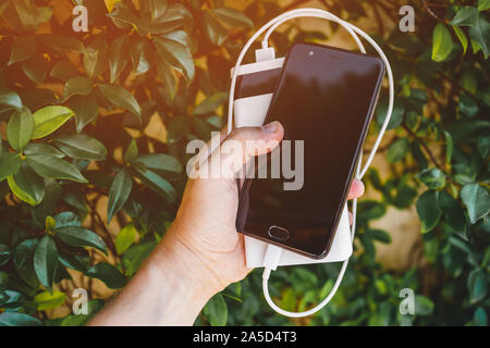 Male hand holding mobile phone avec tarification externe de l'énergie de la batterie, recharge banque smartphone dans travel concept Banque D'Images