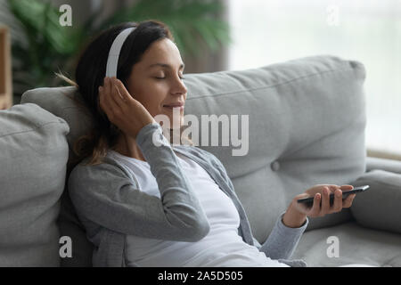 Ambiance young mixed race girl sitting on couch avec écouteurs. Banque D'Images