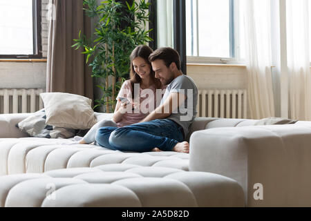 Heureux couple in love relaxing on couch, à l'aide de téléphone Banque D'Images