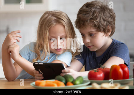 Curieux petit fille et garçon avec phone in kitchen Banque D'Images