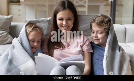 Mère heureuse avec des enfants couverts de couverture chaude reading book Banque D'Images