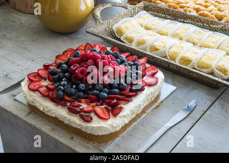 Temps de thé gâteau multiple de baies sur gâteau de crème éponge servi à l'heure du thé avec d'autres gâteaux et desserts dans un cadre rustique avec des couteaux de service. Banque D'Images