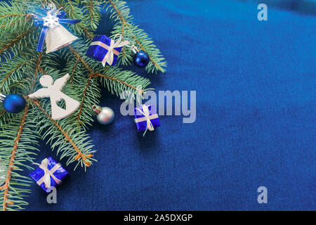 Noël arrière-plan en bleu avec une branche d'arbre de Noël décoré avec des boîtes-cadeaux, cloches et un ange blanc figure. Copier l'espace. Banque D'Images