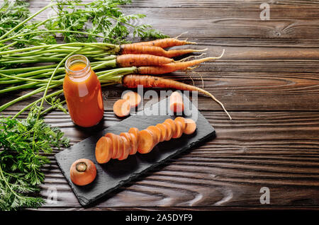 Vue rapprochée au jus de carotte bio végétarienne fraîche en bouteille sur table de cuisine en bois Banque D'Images