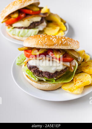 Deux hamburgers faits maison avec une escalope de viande juteuse, parmesan, salade, tomates et pommes de terre sur un fond clair. Shot verticale Banque D'Images