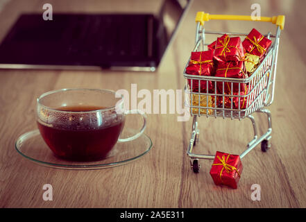 Achats de Noël en ligne. L'image d'un panier avec ordinateur portable, carte bancaire et un verre de thé. Concept. Shopping pratique sans quitter yo Banque D'Images
