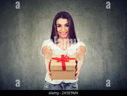 Portrait of a cute smiling girl donner un cadeau fort looking at camera isolé sur fond de mur Banque D'Images