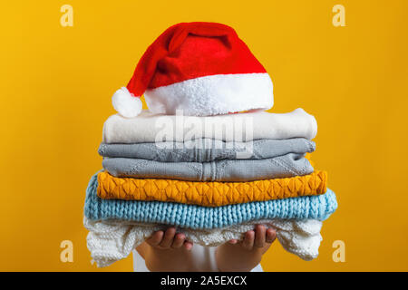 Une femme est titulaire d'une pile de vêtements en tricot chaud, Santa hat est en haut. L'hiver et Noël concept. Banque D'Images