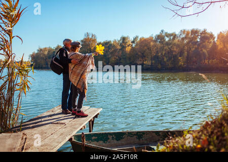 Saison d'automne. Famille Senior couple walking par automne lac. Heureux l'homme et la femme profitant du paysage naturel et hugging on pier Banque D'Images