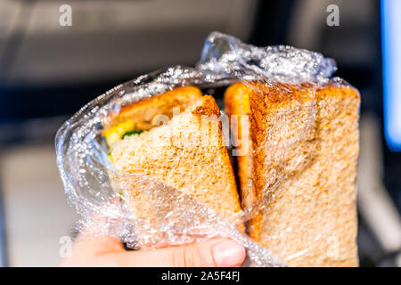 Gros plan du hand holding enveloppés dans du plastique pain de grains de blé entier en croûte avec vol de l'avion et le remplissage de légumes comme repas vegan Banque D'Images