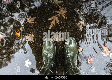 Les pieds dans des bottes en caoutchouc vert olive debout dans une flaque d'eau avec les feuilles tombées. Banque D'Images