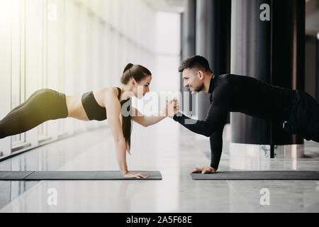 Young couple working out ensemble dans une salle de sport . Faire des exercices planche tout en maintenant l'autre pour une main. Banque D'Images