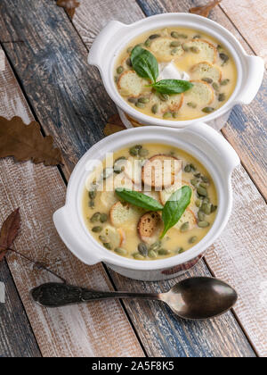 Deux portions de légumes soupe crème d'automne, croûtons, graines de potiron et d'épinards frais sur un fond rustique. Shot verticale Banque D'Images