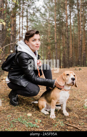 Jolie jeune femme brune caresses mignon chiot beagle, assis sur des squats durant le frisson dans l'environnement naturel Banque D'Images