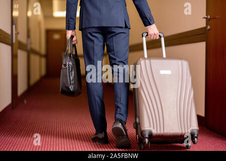 Vue arrière des jeunes hommes d'affaires en litige portant sac à main en cuir noir et suitcase tout en se déplaçant le long du corridor de Banque D'Images