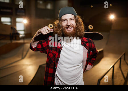 Taille portrait de patineur barbu souriant à la caméra à tout en se posant en milieu urbain Parc de patinage, copy space Banque D'Images