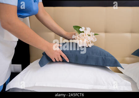 Femme de chambre professionnel penché au-dessus de lit tout en mettant des fleurs fraîches sur le dessus de l'oreiller tout en préparant à manger pour les clients Banque D'Images