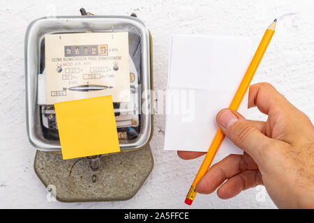 Compteur d'électricité et de papier blanc à la main. Un dispositif de mesure de la consommation de courant électrique. Fond clair. Banque D'Images