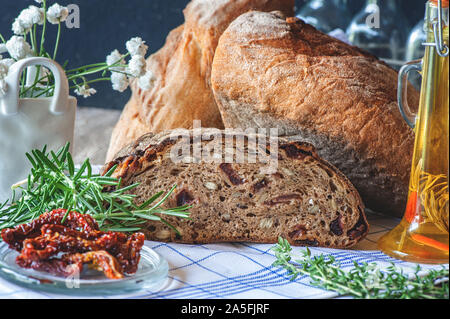 Pain de seigle fraîchement cuits avec des graines et raisins secs sur sans levain levure avec tomates séchées et d'herbes aromatiques de l'huile. Gâteau fait maison. Banque D'Images