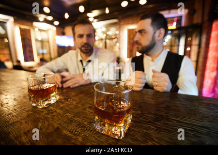 Portrait de deux hommes d'ébouriffé de l'alcool au bar après le travail, l'accent sur deux verres de whisky sur le comptoir, copy space Banque D'Images