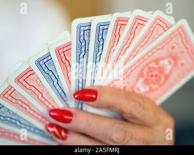 Cartes à jouer en bleu et rouge avec design l'arrière alignés dans une main féminine avec des clous laqué rouge. Se concentrer sur le reste, Point light Bookeh. Close-up Banque D'Images