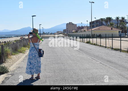 Retour de vacances en tourisme femelle palmier robe d'impression photo prise avec un téléphone mobile de la plage de sable de la promenade dans le sud de la France. Banque D'Images