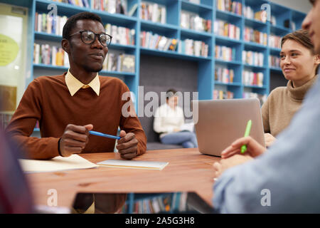 Portrait de l'homme afro-américain smart smiling heureusement tout en étudiant avec groupe d'étudiants en bibliothèque, copy space Banque D'Images