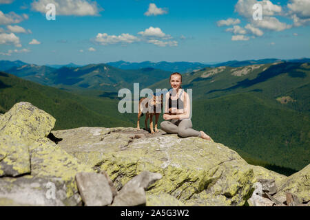 Fille avec un chien en haut d'une montagne de regarder un beau paysage et les bras ouverts. Banque D'Images