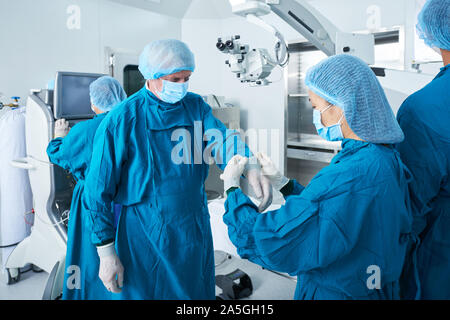 Aider l'assistant chirurgien de porter des gants en latex si vous vous trouvez dans la salle d'exploitation Banque D'Images