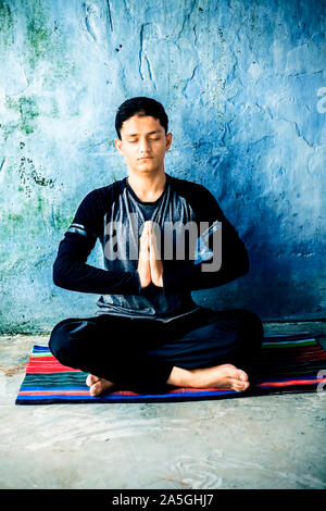 Pose facile ou Sukhasana effectuée par un jeune homme en train de faire sur le tapis coloré en portant des vêtements noirs. Banque D'Images