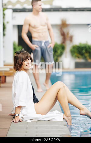 Belle jeune femme assise sur le bord de piscine et l'eau éclabloussures Banque D'Images