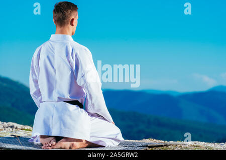 Maître de karaté de méditer au sommet d'une montagne portant des kimono tout en regardant le lac de montagne. Banque D'Images