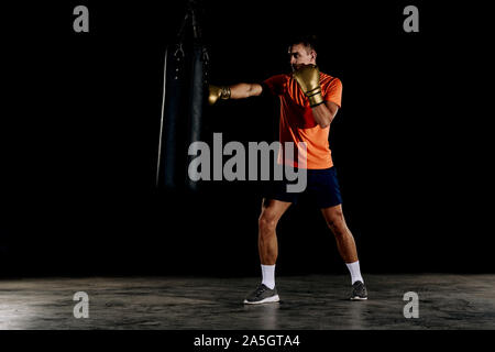 Silhouette male boxer de frapper un énorme sac de frappe de boxe à un studio. Boxer Homme dur formation Banque D'Images