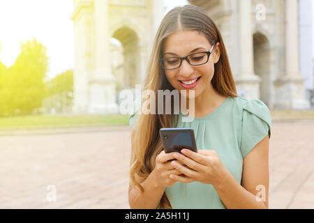 Happy business woman écrire ou lire des messages SMS en ligne sur un téléphone intelligent tout en se tenant dans la ville. Banque D'Images