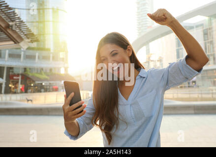 Femme d'affaires commencer la journée avec de bonnes nouvelles sur son téléphone intelligent. Heureux succès femme célèbre piscine acclamations et élever son poing jusqu'à l'exultation Banque D'Images