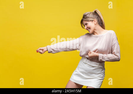 Vue latérale du profil d'assurance positive jeune femme avec les cheveux clairs en blouse beige tirant debout avec le geste, beaucoup d'efforts face à l'expression. Banque D'Images