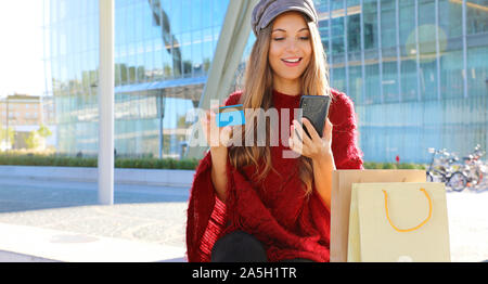 Portrait of happy shopper femme de payer en ligne avec carte de crédit assis sur un banc à l'extérieur. Banque D'Images