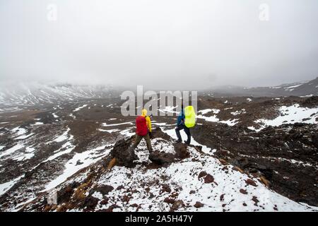 Les randonneurs debout sur des pierres, chemin de randonnée alpine Tongariro Crossing dans la neige sur des champs de lave, Parc National de Tongariro, île du Nord, Nouvelle-Zélande Banque D'Images