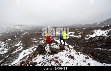 Les randonneurs debout sur des pierres, chemin de randonnée alpine Tongariro Crossing dans la neige sur des champs de lave, Parc National de Tongariro, île du Nord, Nouvelle-Zélande Banque D'Images