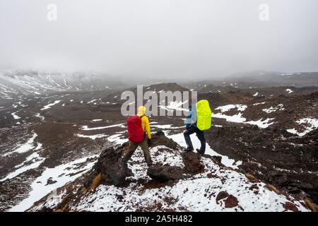 Les randonneurs debout sur des pierres, chemin de randonnée alpine Tongariro Crossing dans la neige sur des champs de lave, Parc National de Tongariro, île du Nord, Nouvelle-Zélande Banque D'Images