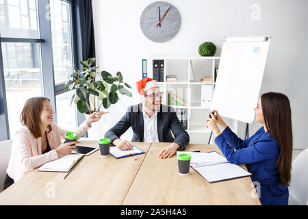 La célébration de Noël ou Nouvel an. Les travailleurs de bureau. Jeune homme et femmes s'asseoir ensemble et de table. Prendre des photos sur le téléphone appareil photo. Avoir du plaisir. Maison de Vacances Banque D'Images