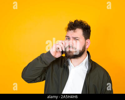 Cool man with smartphone, barbe noire et les cheveux noirs se posant en face de fond orange et de faire différentes expressions Banque D'Images