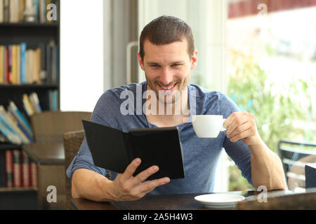 Vue avant portrait d'un homme heureux de lire un livre assis dans un café Banque D'Images