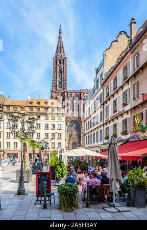 Les gens en train de déjeuner à la terrasse d'une brasserie sur la place Gutenberg à Strasbourg, en France, avec la cathédrale Notre-Dame à la distance. Banque D'Images