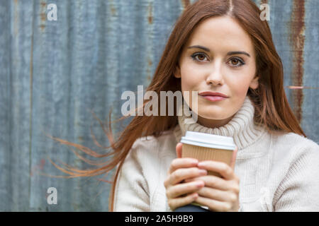 Portrait d'une belle jeune fille ou jeune femme aux cheveux rouges portant un cavalier blanc de boire du café à emporter Banque D'Images