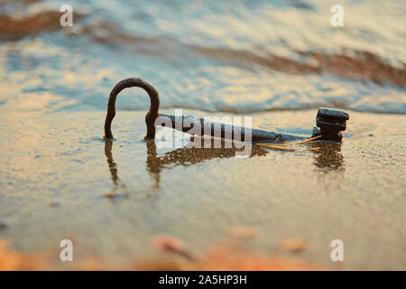 Un trésor perdu old rusty key, couché dans le sable dans le surf sur la plage. La notion de chance et de richesse inattendue. Banque D'Images