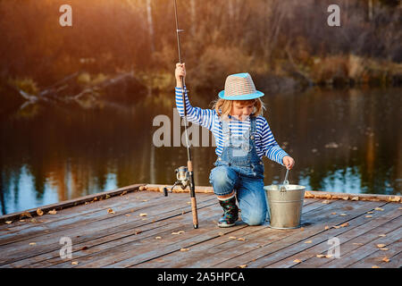 Une petite fille avec une canne à pêche ressemble à la prise de poissons dans un seau. Banque D'Images