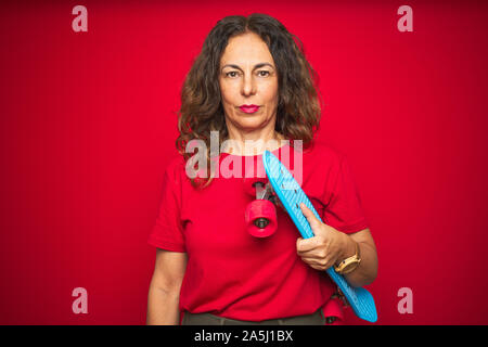 L'âge moyen du patineur senior woman holding skateboard rouge sur fond isolé avec une expression confiante face à la pensée intelligente grave Banque D'Images