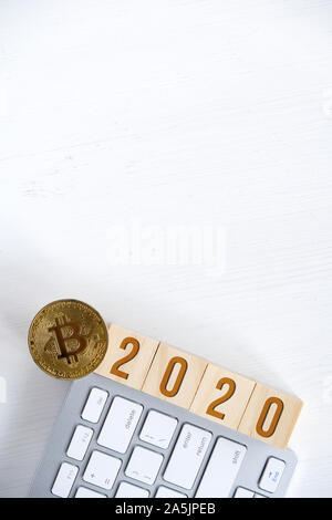 Les numéros de 2020 avec Bitcoin sur les cubes en bois sur un clavier blanc avec un fond de bois. Le succès de cryptocurrency dans la nouvelle année. Mise à plat. Copie Banque D'Images