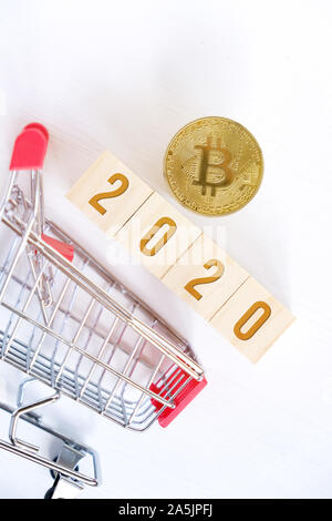 Les numéros de 2020 avec Bitcoin sur les cubes en bois sur un fond en bois blanc avec un chariot. Le succès dans l'achat d'cryptocurrency dans la nouvelle année. La verticale. Fla Banque D'Images